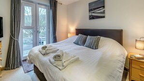 Hotellihuone, jossa on suuri sänky, yöpöytä lampun kanssa, televisio ja lasiovesta avautuva näkymä ulos.