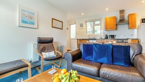 Un salon moderne avec un canapé en cuir, une table à manger ornée de fruits, une chaise et une vue sur la cuisine.