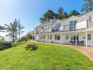 Un bâtiment à deux étages doté d’un balcon, d’un espace extérieur aménagé pour s’asseoir et d’une pelouse verdoyante.