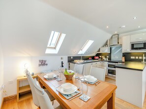 A modern kitchen with a dining area, featuring skylights, white cabinetry, and a wooden dining table set for four. - 2 bedroom accommodation in Seaton (Seaton)