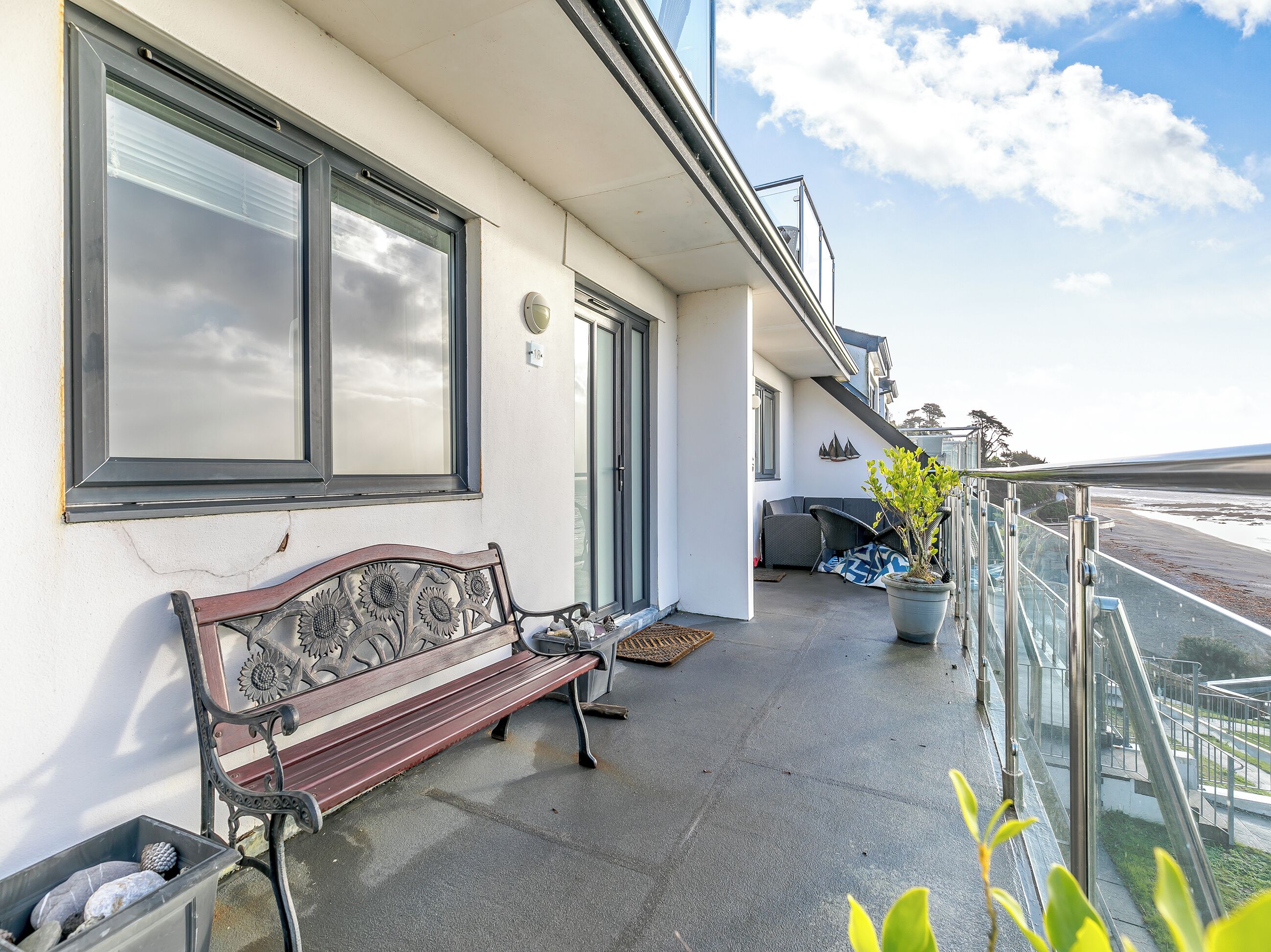 Ein Balkon mit einer Bank, einem Blumentopf und Blick auf den Strand.