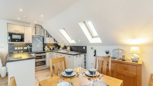 Een moderne keuken met een eethoek, voorzien van dakramen, een gedekte eettafel voor vier personen en een klein bijzettafeltje met een lamp.