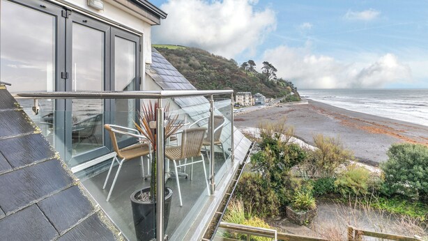 Een modern huis met een glazen balkon met uitzicht op een strand en zee.