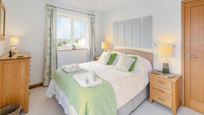 Een keurig opgemaakt slaapkamer met een bed, nachtkastjes, een kledingkast en een raam met gordijnen.