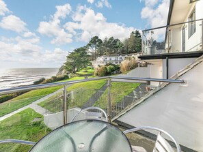 A balcony with a glass railing overlooking a coastal area with houses and greenery. - 2 bedroom accommodation in Seaton (Seaton)