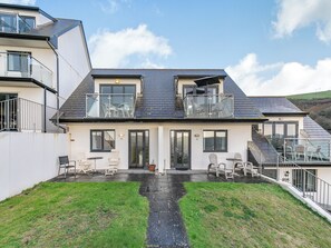 A two-story house with a balcony, a small patio with outdoor furniture, and a grassy yard. - 2 bedroom accommodation in Seaton (Seaton)