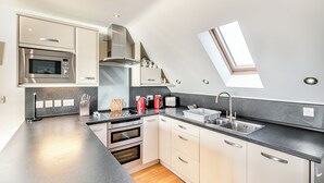 A modern kitchen with a built-in oven, microwave, and stainless steel range hood. - A contemporary house in a peaceful setting, with superb views over the sea. (Seaton)