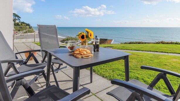 Een terras met een ontbijtgedekte tafel, met uitzicht op de kust.