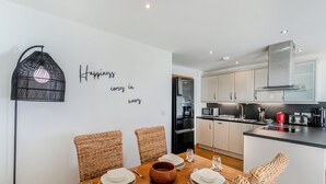 Een moderne keuken met witte kasten, een zwarte koelkast, en een eethoek met rieten stoelen en een houten tafel gedekt voor vier personen.