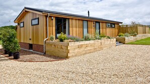 Un bâtiment en bois avec une allée de gravier, des jardinières en bois surélevées où sont plantées des fleurs, et un ciel dégagé.