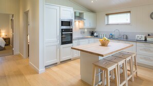 A modern kitchen with white cabinetry, a central island with stools, a skylight, and a window with blinds.