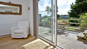 Ein modernes Wohnzimmer mit einem weißen Sofa, einem großen Glasfenster, das auf eine Terrasse führt, und einer Holzbalkendecke.
