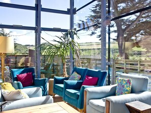 Une pièce lumineuse, baignée de soleil, avec de grandes fenêtres, des fauteuils à revêtement bleu, une table en bois et une plante en pot.