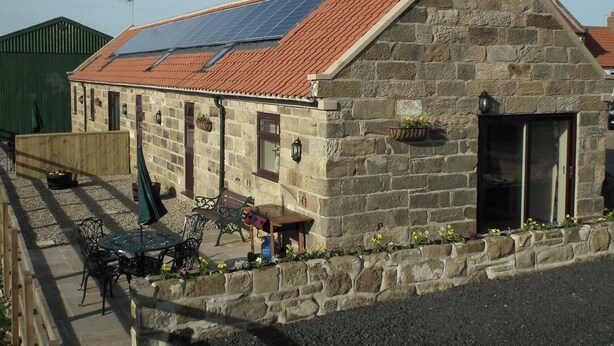 A stone building with a sloped red-tiled roof, a weather vane, and a solar panel. - Byre Cottages**Nr Stokesley (Carlton near Stokesley)