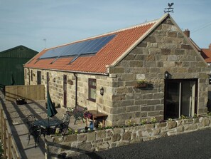 A stone building with a sloped red-tiled roof, a weather vane, and a solar panel. - Byre Cottages**Nr Stokesley (Carlton near Stokesley)