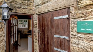 A wooden door with metal hinges and a sign reading "THE NOOK" on a stone wall.