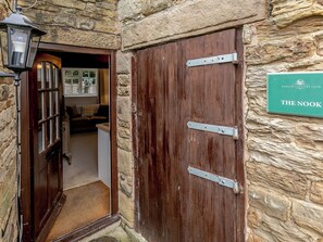 Una puerta de madera con bisagras metálicas y un letrero que dice THE NOOK en una pared de piedra.