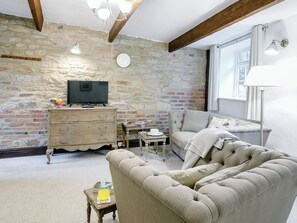 Una sala de estar acogedora con pared de piedra, techo de madera, televisor, sofá y lámpara.
