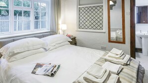 A neatly made bed with pillows and a magazine, a bedside lamp, a window with curtains, a mirror, and a sink.