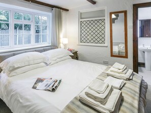 A neatly made bed with pillows and a magazine, a bedside lamp, a window with curtains, a mirror, and a sink.