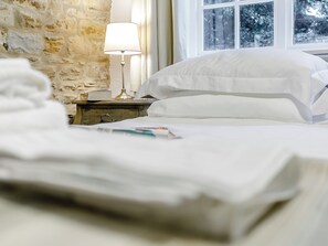 Una cama bien hecha con sábanas blancas, una lámpara de noche y un libro sobre una mesita de madera.
