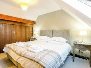 A neatly made bed with a plaid bedspread and folded towels, a wooden wardrobe, and a bedside table with a lamp and books. - Mill Farm Cottages - Cherry Tree (Barlow near Bakewell)