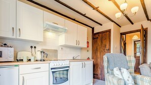 Una cucina compatta con mobili bianchi, un fornello e un forno a microonde. Si apre una porta in legno verso un'altra stanza.