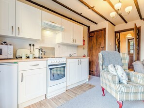A compact kitchen with white cabinets, a stove, and a microwave. There is a wooden door leading to another room. - 4 lovely Cottages situated in the beautiful Derbyshire village of Barlow. (Barlow near Bakewell)