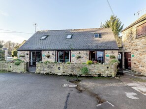 A stone building with a sloped roof, a small porch with potted plants, and a sign indicating a business. - 4 lovely Cottages situated in the beautiful Derbyshire village of Barlow. (Barlow near Bakewell)