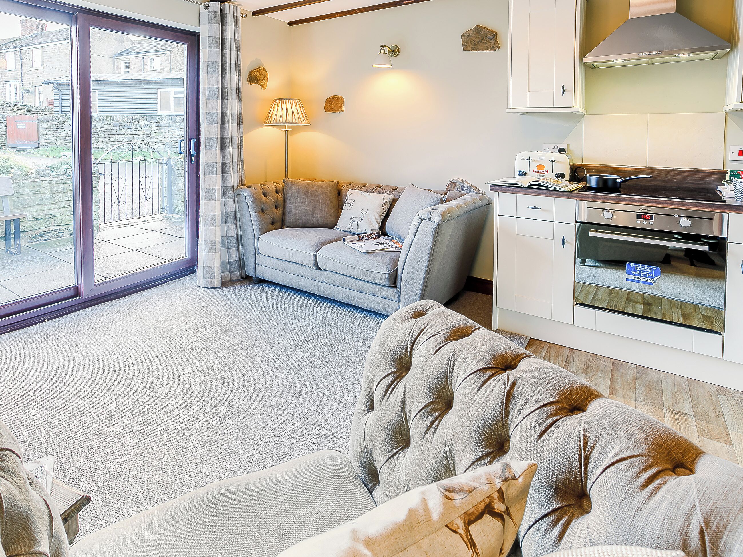 Ein Wohnzimmer mit Sofa, ein Essbereich mit Tisch und Stühlen, eine Küche mit Backofen und ein Blick ins Freie durch ein großes Fenster.