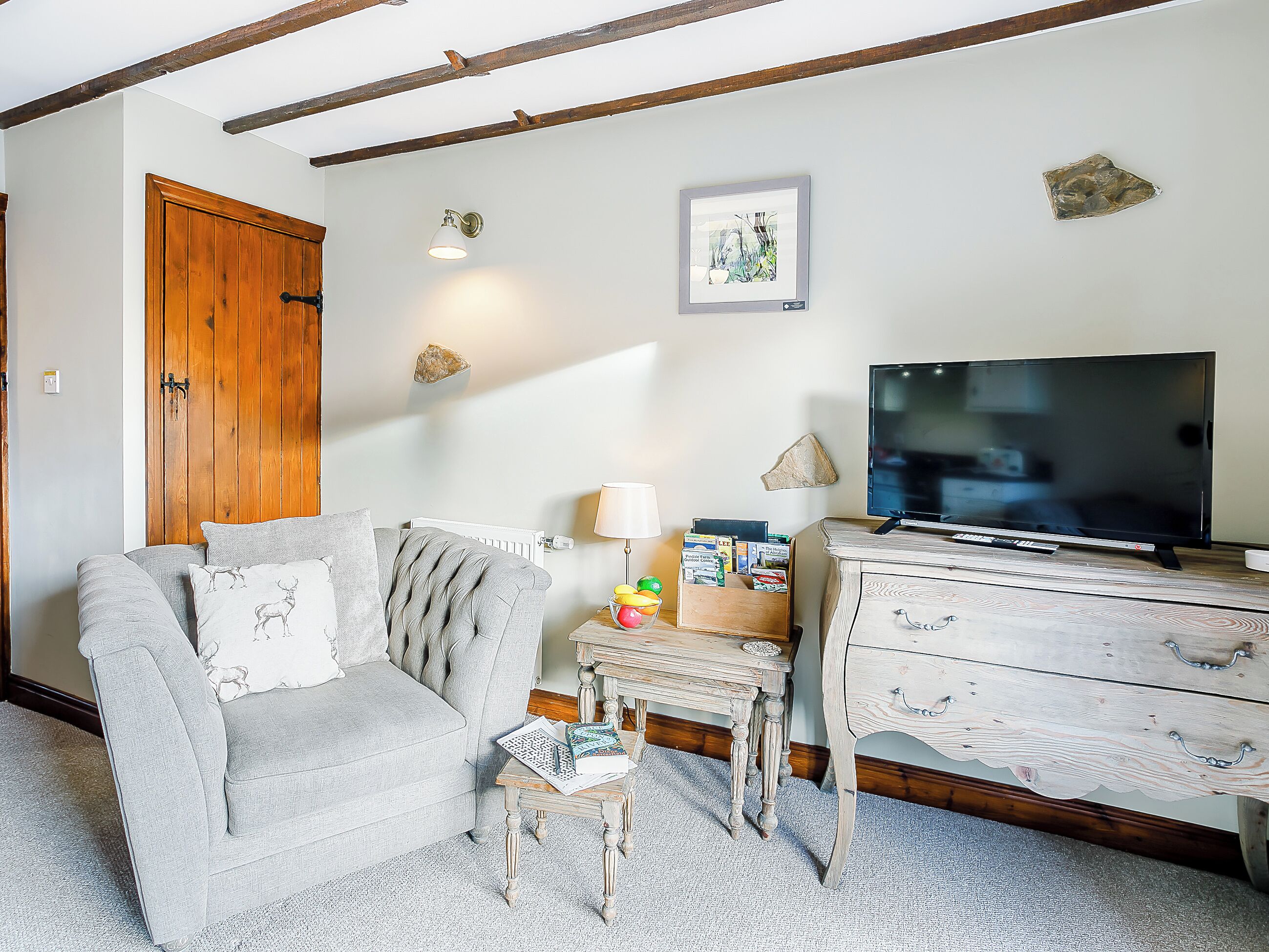 Un salon comprenant un canapé, un téléviseur, une commode en bois et une petite table sur laquelle se trouvent des livres et une lampe.