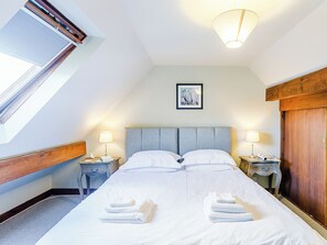 Ein ordentlich bezogenes Bett mit weißen Leinen und Handtüchern, ein gerahmtes Bild an der Wand und ein Oberlicht darüber.
