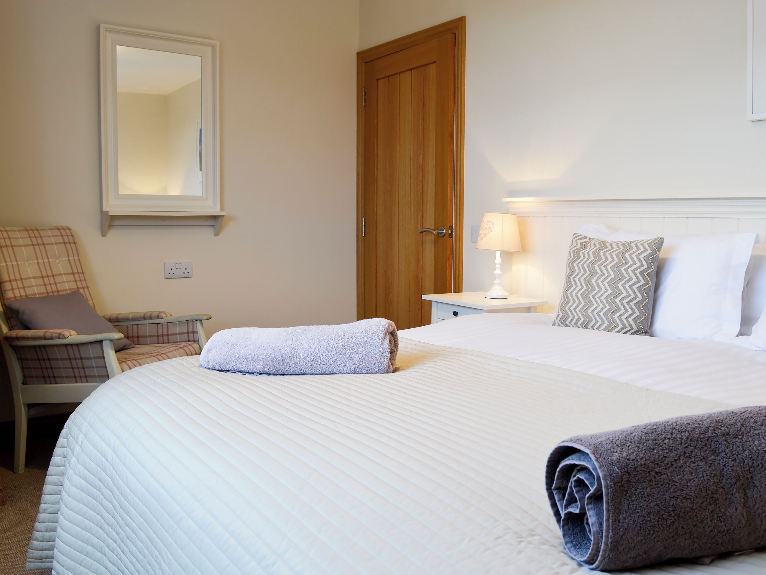 Une chambre d’hôtel avec un lit, une chaise, une table de chevet, une lampe et une porte en bois.