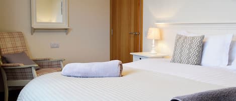 A hotel room with a bed, a chair, a nightstand, a lamp, and a wooden door.