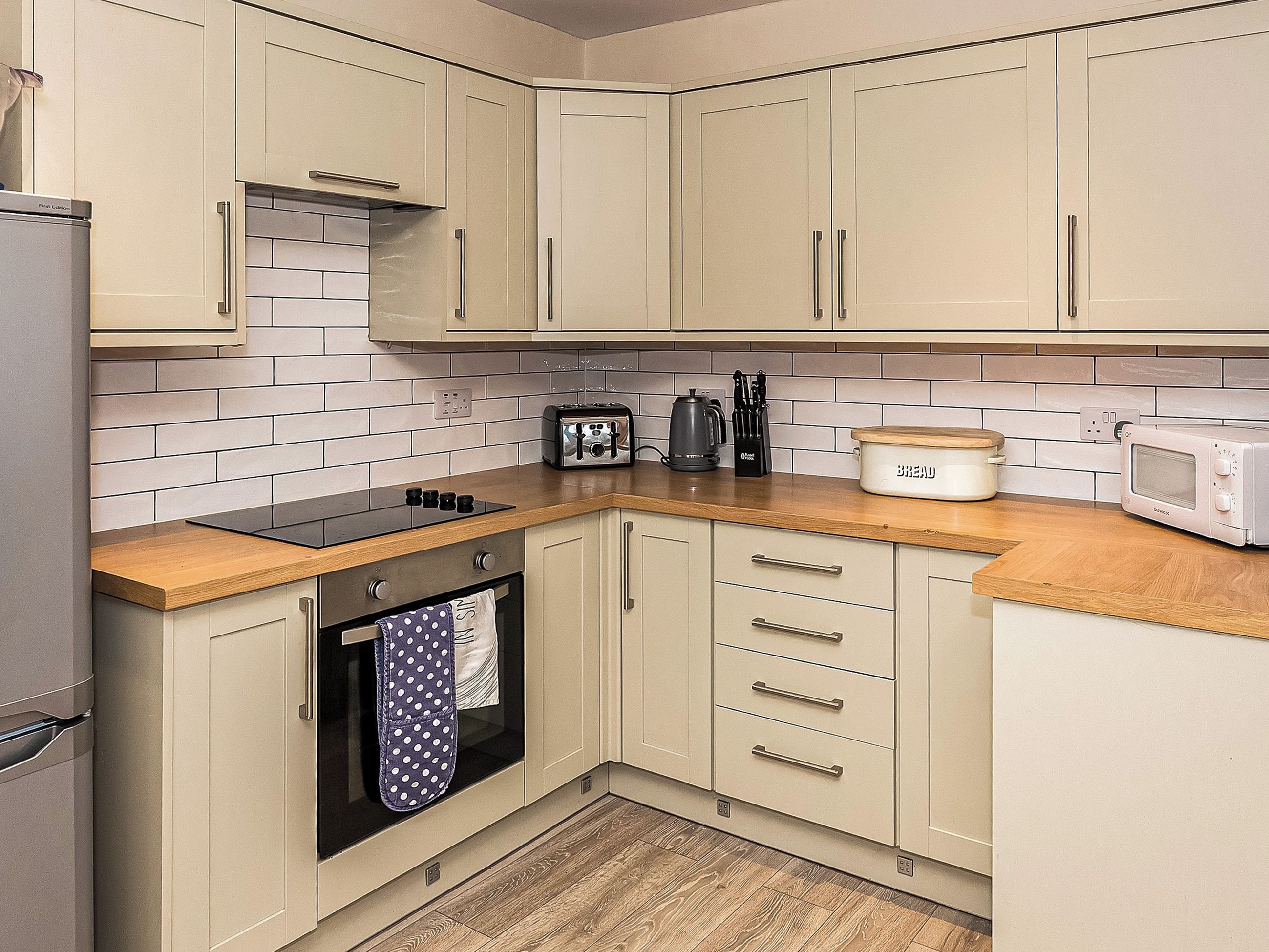 A kitchen with a stove, oven, microwave, toaster, and a bread container.