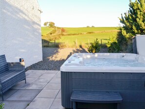 Un bain à remous avec vue sur un paysage rural, une chaise en osier et un mur blanc.