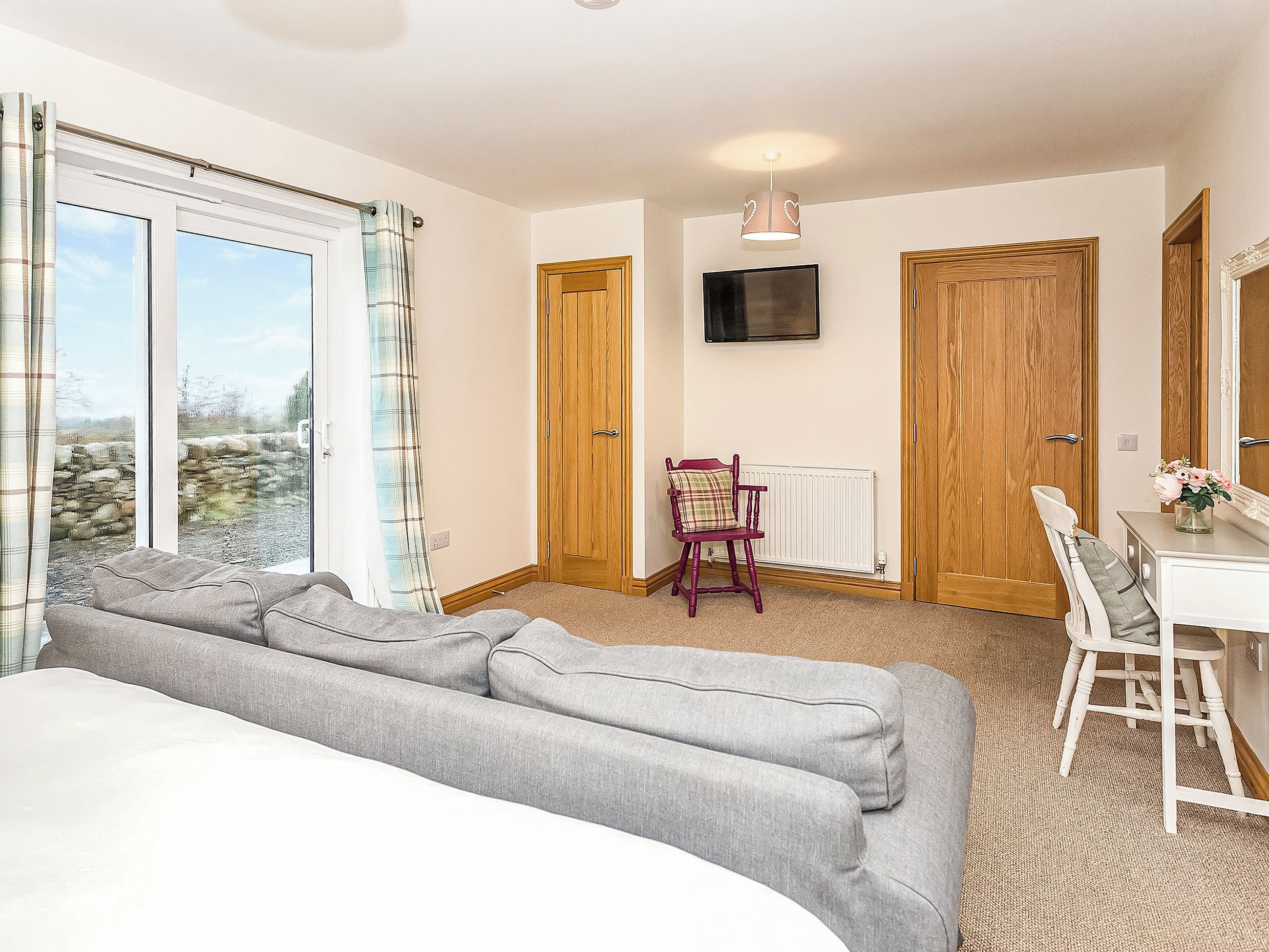 A bedroom with a large window, a sofa, a chair, a TV, and wooden doors.