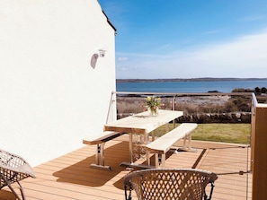 Una terraza de madera con mesa y sillas, con vista a un cuerpo de agua.