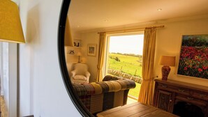 Ein gemütliches Zimmer mit großem Fenster, einem Sessel, einer Couch und einem Holztisch.