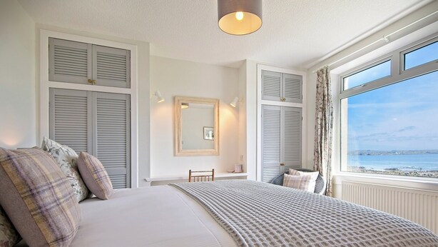 Ein Schlafzimmer mit Bett, Nachttisch, Stuhl, Fenster mit Meerblick und Spiegel an der Wand.