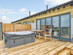 A wooden deck with a hot tub, outdoor seating, and a large sliding glass door leading to a view.