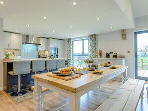 Una cucina moderna con zona pranzo, caratterizzata da un tavolo lungo, sgabelli da bar e vista dalla finestra.