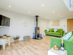 Una sala de estar con chimenea, sofá verde, televisor de pantalla plana y piso de madera.