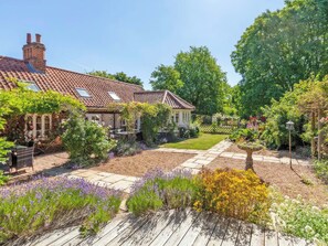 Un jardin avec une maison, une terrasse en bois et une pelouse.