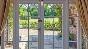Eine weiße Tür mit Fenster, die zu einem Garten mit Ziegelmauer und Pflanzkübeln führt.