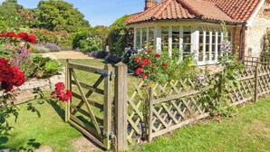 Ein traditionelles Haus mit Ziegeldach, umgeben von einem Holzzaun und einem Garten mit verschiedenen Blumen.