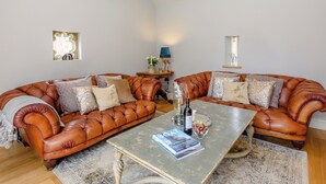 Un salon avec un canapé en cuir marron, une table basse et une petite table d’appoint sur laquelle se trouve une lampe.