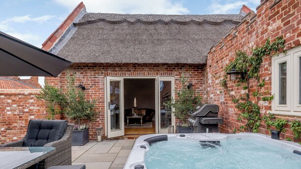Une maison en briques avec un patio, un jacuzzi et du mobilier d’extérieur.
