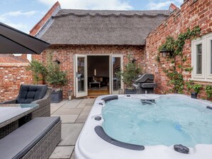 Een bakstenen huis met terras, een bubbelbad en tuinmeubilair.