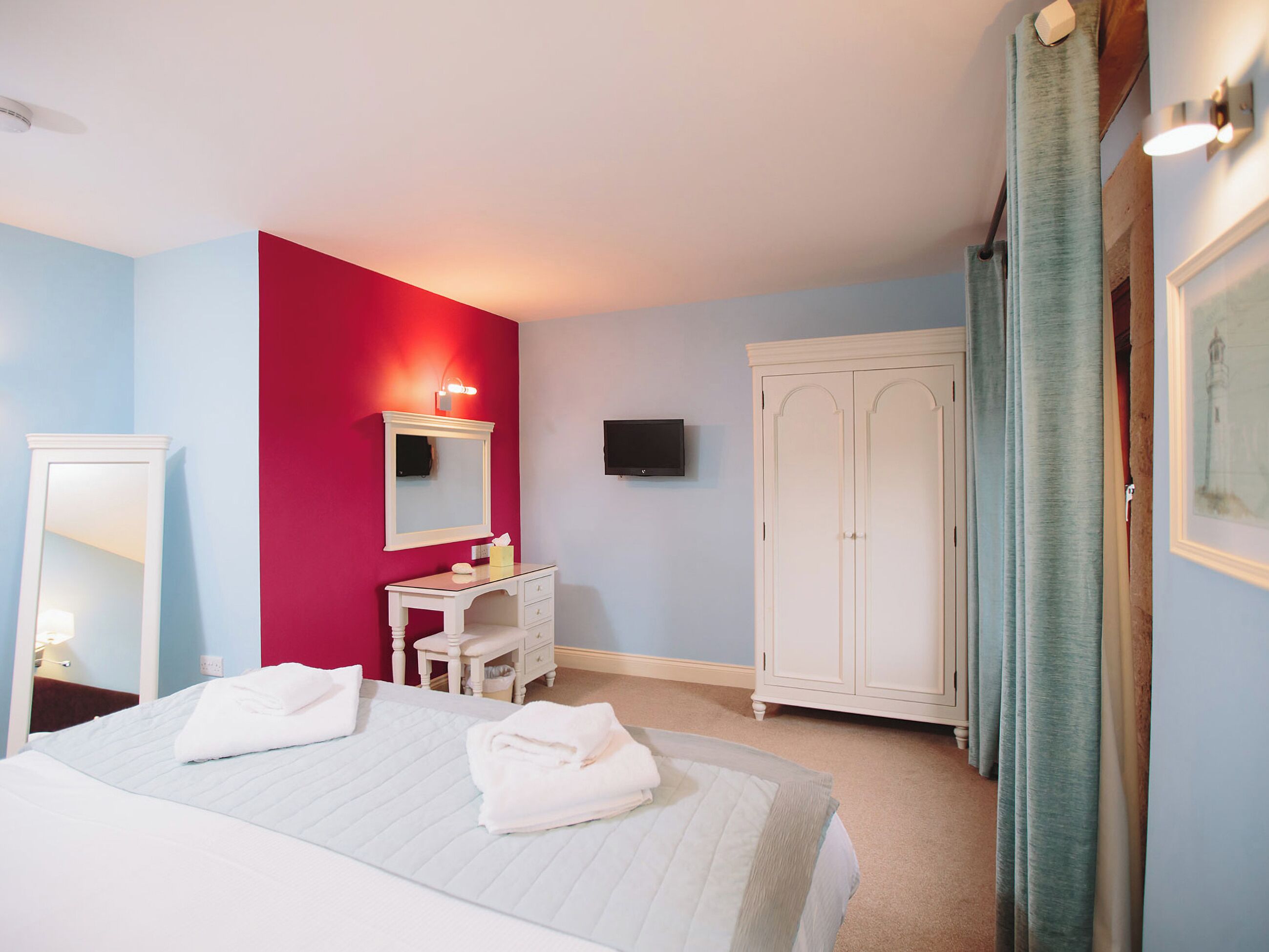 Una habitación de hotel con cama, escritorio, espejo, armario y televisor.
